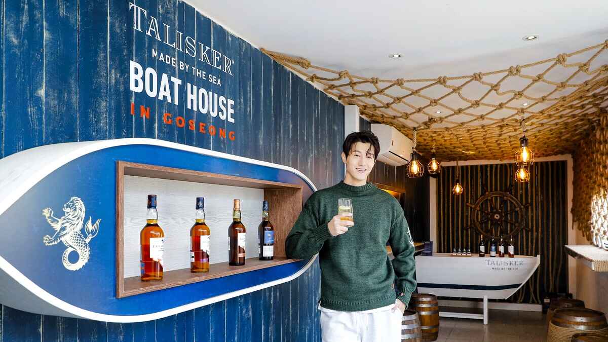 Actor Li Ki-Woo stands in front of a bar counter that says 'Talisker Made by the Sea: Boathouse in Goseong', featuring Talisker whiskies.